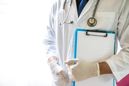A doctor is working in the hospital, he is wearing a brown stethoscope and holding the clipboard for...