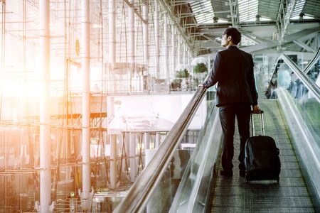 Elegant asian businessman checking email on mobile phone while walking with suitcase inside airport, experienced male employer using cell telephone while waiting for taxi car coming before work travelの写真素材