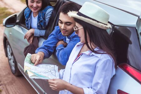 Happy young Asian friend looking to the map traveling by the eco car on vacation holiday with travel road trip. Main focust is a man. Car travel concept.の写真素材