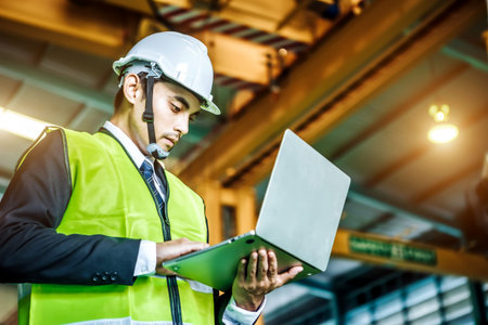 Asian engineer man wearing white helmet and using laptop to monitoring the production status....