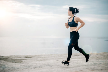 Sporty young Asian woman running on sidewalk in morning. Health conscious concept with copy space.