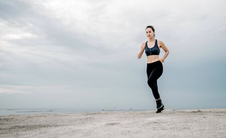 Sporty young Asian woman running on sidewalk in morning. Health conscious concept with copy space.の写真素材