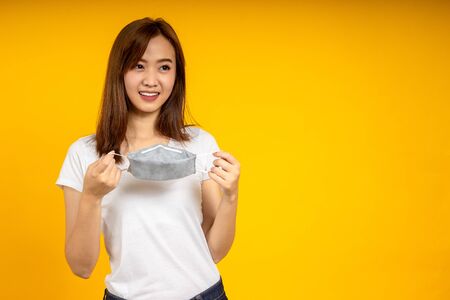 Asian woman took off hygienic mask to protect virus, COVID 19 or Colona Virus infection and dust PM 2.5 pollution isolate on yellow backgroundの写真素材