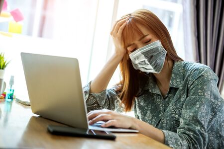 Young asian woman wearing mask protect covid-19 feeling strain fatigue and have a fever during working with laptop in her home. work from home conceptの写真素材