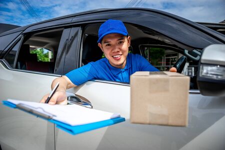 Asian delivery man in blue t-shirt on car send the box and document to sign. Delivery man concept.の写真素材