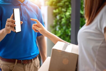 A young Asian deliveryman is delivering parcel to house her to sign to receive the product After she ordered online during the outbreak of the coronavirus or Covid-19 virus.の写真素材