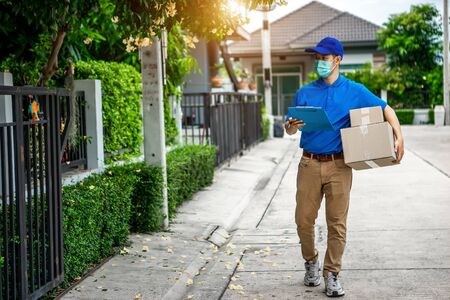 Asian delivery man in blue t-shirt carrying parcel box and document to sign in front of customer home. Delivery man concept.の写真素材