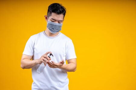 Asian man is wearing a white t-shirt and wearing a mask, holding an alcohol spray bottle. He was spraying it for cleaning  or washing his hands to prevent an outbreak of coronavirus or covid-19.の写真素材
