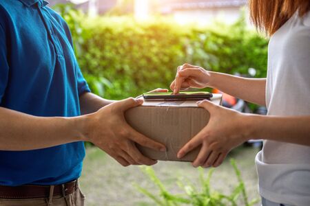 A young Asian deliveryman is delivering a package to customer in front of her house her to sign to receive the product After she ordered online during the outbreak of the coronavirus or Covid-19 virus.の写真素材