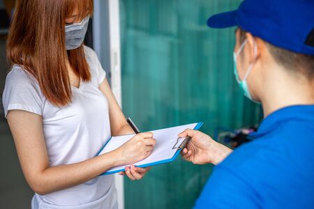 Asian deliveryman delivering package parcel food to customer in front of her house and sign to receive the box after she ordered online by application during the outbreak of the coronavirus or Covid-19 virus.の写真素材