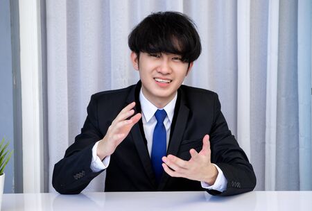Asian business man wearing suit, enjoying and smiling with chat and holding video call with clients partners.の写真素材
