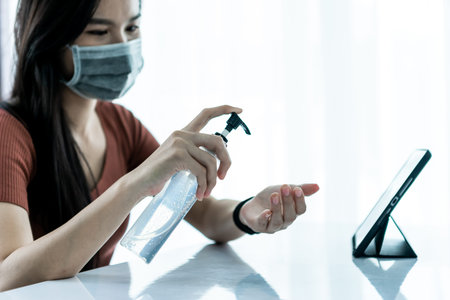 Asain woman cleaning hand and using laptop, smarthphone and tablet to work from home and meeting online via internet with customer from home. Work from home or E-Learning concept.の写真素材