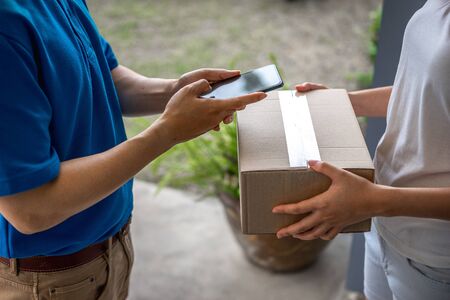 Asian deliveryman is delivering parcel to house her to sign to receive the product After she ordered online during the outbreak of the coronavirus or Covid-19 virus.の写真素材