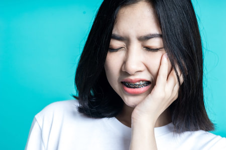 Teenage woman wearing braces and she is having a toothache isolate background