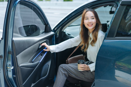 Asian business woman gets out of car and holding phone and coffee cup, right-hand drive, left-hand traffic, business lady, white business class luxuryの写真素材