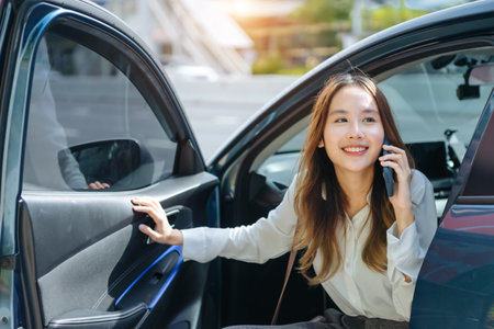 Asian business woman gets out of car and holding phone and coffee cup, right-hand drive, left-hand traffic, business lady, white business class luxuryの写真素材