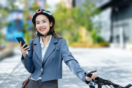 Young Asian businesswoman wearing helmet and standing on a city street with bicycle looking at phone.の写真素材