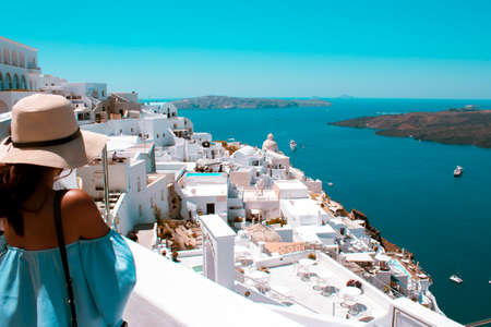 Close up asian girl with a hat. Arial panoramic view of santorini (thera) the white town. Sea and little island in the background.の写真素材