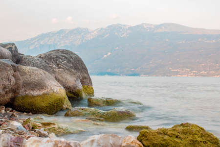 Lago di Garda ( Garda lake ) at sunset with light pink - a mountain in background. Long exposure time - little wavesの写真素材