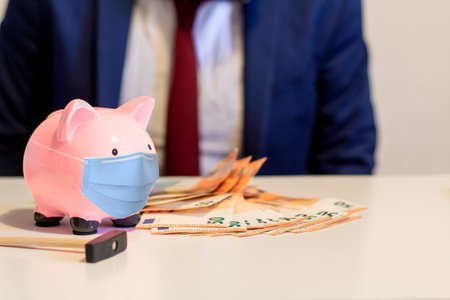 Close up of piggy bank, wearing protective face mask. Money saving concept in time of virus...