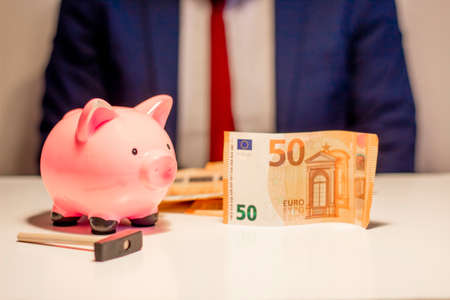 Business man showing in hand fifty euro banknote and holding piggy bank. Financial and money saving conceptの写真素材