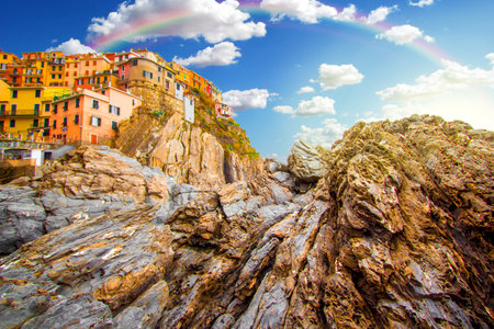 Rainbow on Manarola in cinque terre on the mountain near mediterranean sea in liguria - Italy. Sunny cloudy sky with rainbow. Traditional italian architectureの写真素材
