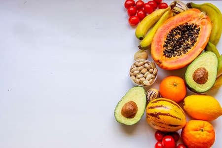 Healthy food clean eating selection: orange yellow fruit, vegetable, seeds, superfood, avocado, papaya on white concrete backgroundの写真素材