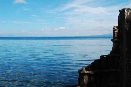 blue water bay and blue sky seen beyond ruins of concrete wallの写真素材