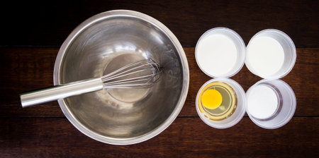 Ice cream making ingredients on plastic bowl and steel whisk.