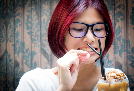 Red hair asian nerdy girl having chocolate shake and macaronsin vintage cafeの写真素材