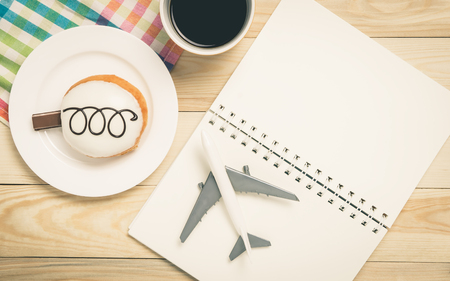 Travel planing in a colorful pastel cafe. Vacation planning book blank page with plane and donut. Planning your colorful vacation trip on a cafe table with coffee and donut.の写真素材