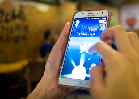 Bangkok, Thailand - August 6, 2016: A girl is playing Pokemon Go on her samsung mobile in a restaurant.のeditorial素材
