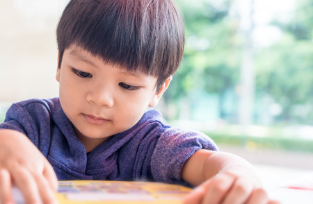 little Asian boy is reading a picture bookの写真素材