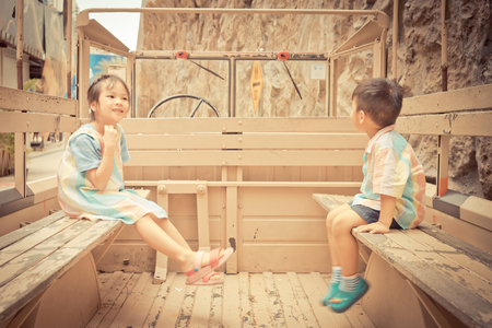 Happy Asian children are riding on a truck. Smiling Asian siblings sitting on different side on a military truck with copy space in the middle.の写真素材