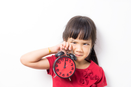 Asian girl is angry and wanting to go to bed. Girl holding a clock counting at mid night to requesting Bed Time. Sleepy tired little girl need to go bed to sleep.の写真素材