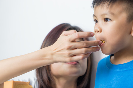 Mother is feeding her son Cake using her finger. Asian boy is having orange cake.の写真素材