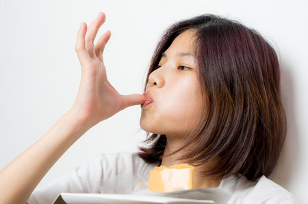 Japanese girl is deeply enjoying by lick the cake on her finger, on white background.の写真素材