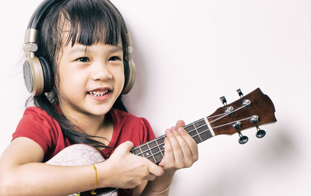 Asian girl is practicing guitar and wearing headphone. Little Musician is smiling while playing her guitar on white background.の写真素材