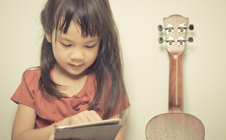 little girl is learning how to play guitar on Internet using her tabletの写真素材