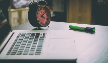 Messy office table with alarm clock for deadline reminder.