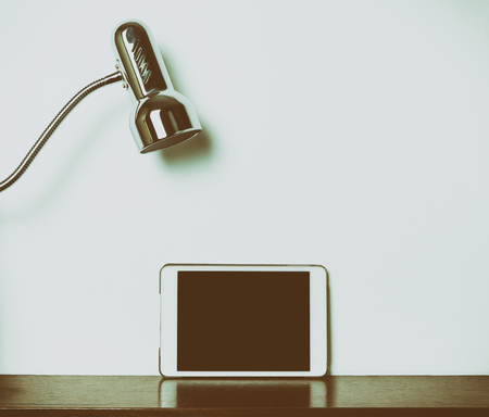 Blank tablet screen on wooden table with a lamp on topの写真素材
