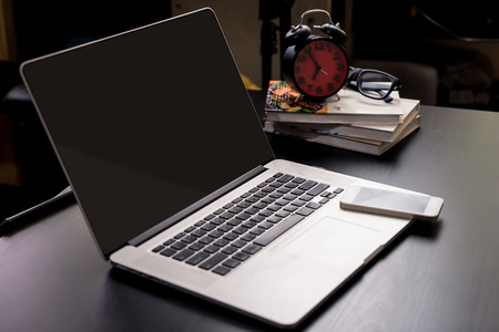 Blank laptop screen on office table with clock and smart phone.の写真素材