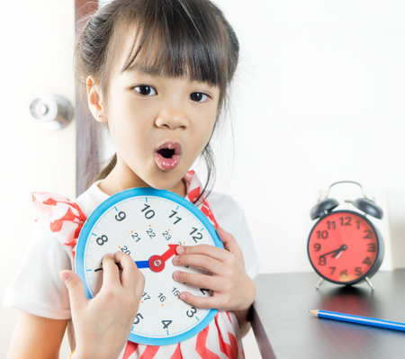Little asian girl holding toy clock for school time