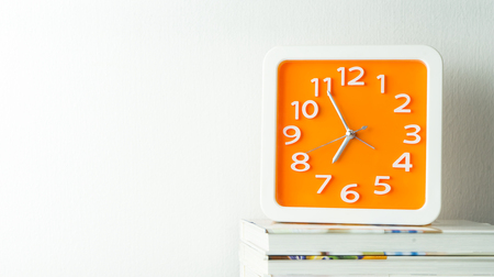 Orange clock on stacked book with white copy space wallの写真素材