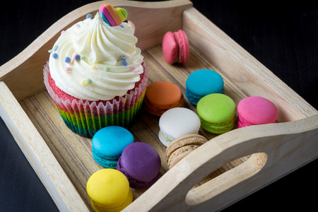 Colorful Macaron cookies and cupcake on wooden trayの写真素材