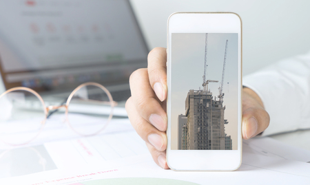 Business man is holding smartphone with construction industry conceptの写真素材