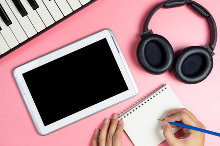 Music Songwriter is writing on a notebook with blank tablet screen for music application mock upの写真素材
