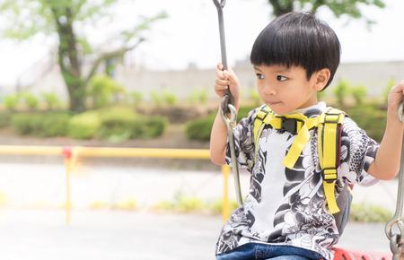 Asian boy swinging in playground with bright copy spaceの写真素材