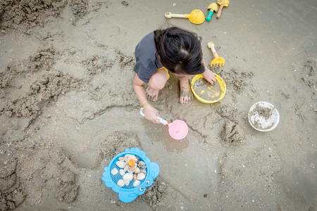 Asian girl is playing with sand toys on the beachの写真素材