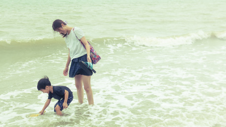 Asian Mother and Son is playing with the wave on the beachの写真素材